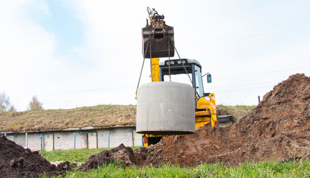 Tractor at a construction site carries a concrete ring for a well