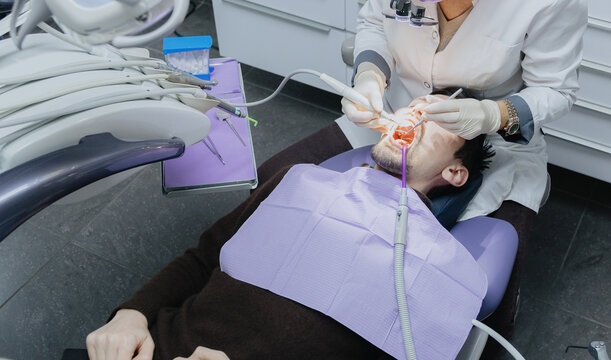 An unrecognizable dentist performs a professional cleaning procedure on a guy's front teeth.