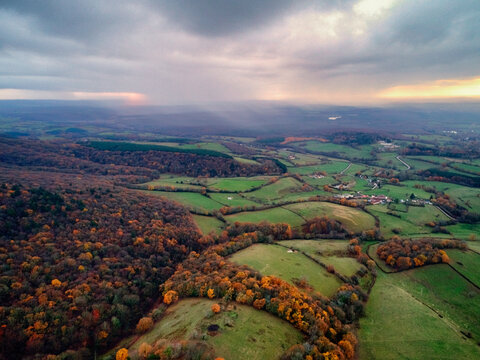Aerial view of rolling green hills and autumnal forests meet under a sky of soft light and brooding clouds, Morvan, France.