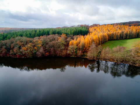 Aerial view of the contrasting autumn foliage paints the landscape with vibrant hues along the tranquil waters of Morvan's lake, Morvan, Morvan, France.