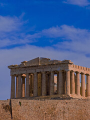 Fototapeta premium Parthenon, monumental symbol of Western civilization, stands atop the Acropolis hill against a vast, blue sky scattered with clouds, emphasizing the historical significance of the ancient structure.