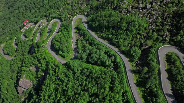Top-down aerial view of Trollstigen hairpin turns in Norway. The winding road cuts through forested mountains, showcasing engineering and natural beauty.