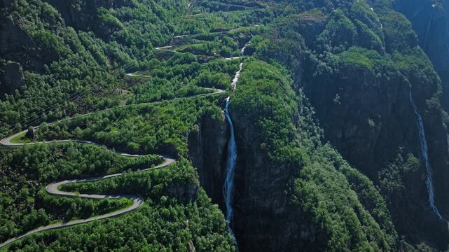 Drone footage follows Trollstigen road climbing steep mountains near Geirangerfjord. Narrow curves, waterfalls and rugged terrain define this famous scenic route.