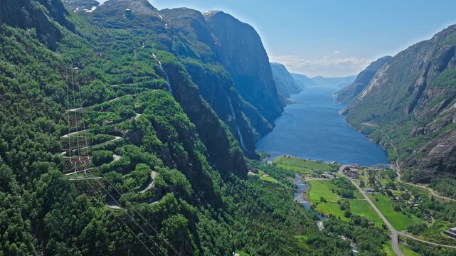Wide aerial panorama of Trollstigen winding through green mountains near Geirangerfjord Norway. Scenic drone view highlights iconic hairpin turns and alpine landscape in summer.