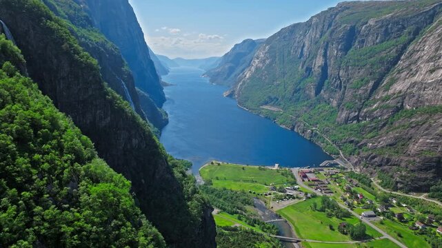 Scenic aerial view over Geirangerfjord and valley village in Norway. Drone shot captures deep blue fjord water, steep cliffs and peaceful rural landscape during sunny summer weather.