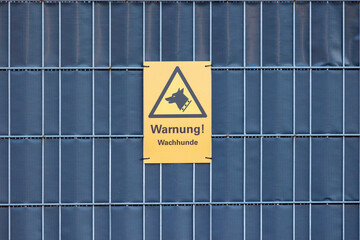 Yellow warning sign with the inscription "Warning! Guard dogs" on a metal fence