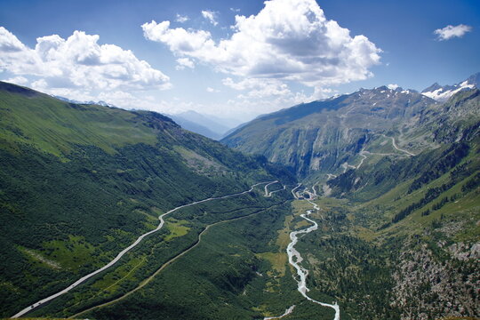 Mountain valley with winding river and road under partly cloudy sky