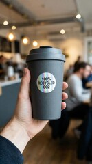 carbon dioxide sustainability monitoring concept. Hand holding a recycled coffee cup in a cafe setting.
