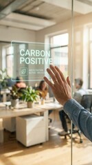 carbon dioxide sustainability monitoring concept. Hand reaching for a glass door with "Carbon Positive" sign in an office setting.