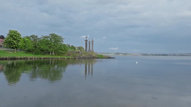 Calm drone view over Hafrsfjord near Sverd i Fjell monument in Stavanger Norway. Peaceful coastal water and green shoreline under cloudy skies, ideal for travel and nature backgrounds.