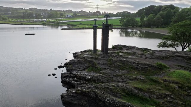 Side angle drone view of Sverd i Fjell monument by Hafrsfjord Stavanger. Tourists gather near the swords, exploring Norwegian history in peaceful weather.