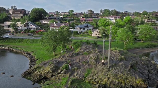 Drone orbit around Sverd i Fjell monument with Stavanger neighborhood nearby. Tourists walk and take photos while visiting the iconic Viking landmark.