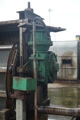 Detail of robust industrial heavy machinery featuring a prominent green motor and complex gear mechanism, operating within a manufacturing or processing facility environment