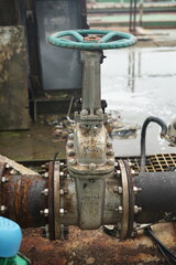 Industrial valve with large handwheel on large rusty pipes in an outdoor setting