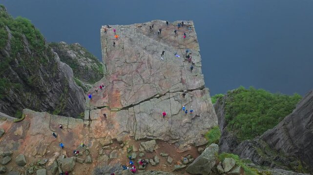 Tourists enjoy Pulpit Rock cliff Preikestolen Norway. Visitors sit and walk across the famous rock formation, enjoying the dramatic drop and peaceful scenery during a summer hike.