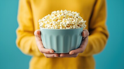 Freshly Popped Popcorn in Bowl Held by Person Against Bright Blue Background