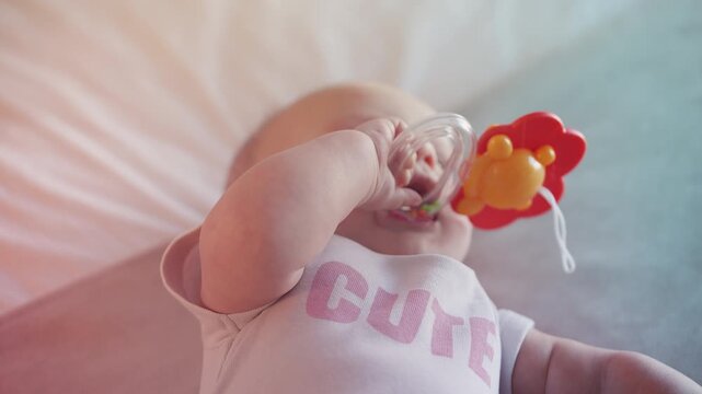 Adorable baby girl chewing colorful teether toy while playing on bed