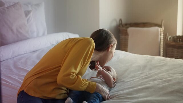 Young mother playing with adorable baby girl on bed, healthy infancy and bonding