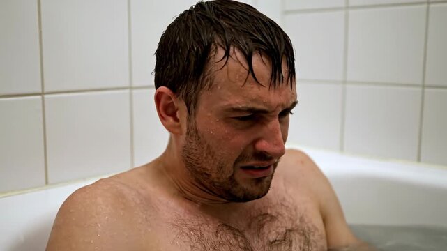 Man in bathtub shivering from cold water or pain
