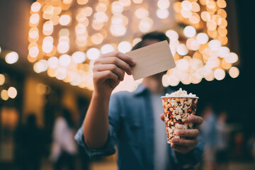 Man holding cinema ticket and popcorn on solo date under glowing lights, enjoying movie night atmosphere with excitement and anticipation for entertainment experience