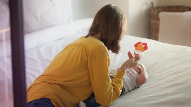 Happy mother entertaining newborn baby girl with colorful teether toy
