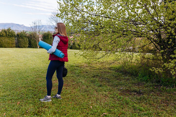 rear view of a woman standing in the park with fitness mat