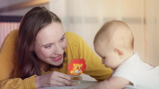 Happy mother entertaining newborn baby girl with colorful sensory toy