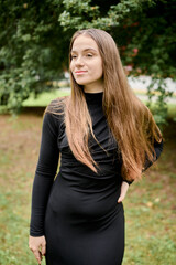 Obraz premium Young woman in black dress posing outdoors near greenery