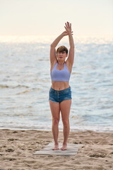Young woman practicing yoga stretch on Baltic Sea beach at sunrise