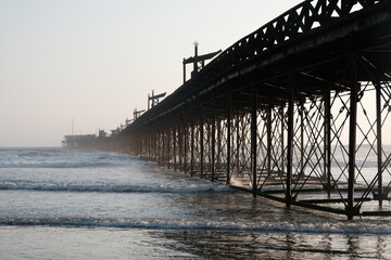 Pimentel old historic iron pier with detailed structure reflecting on the ocean water, waves breaking against its supports
