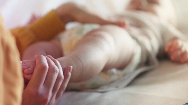 Mother playing with newborn daughter, touching tiny baby feet affectionately