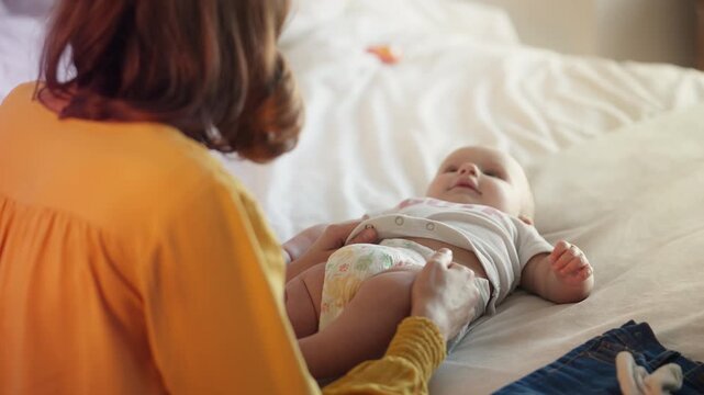 Happy mother changing diaper on active newborn girl, baby care concept