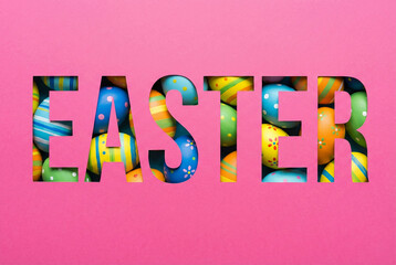The word EASTER cut out from pink paper revealing colorful eggs underneath concept