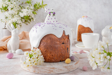 Easter sweet bread or Easter cake - Paska with sugar glaze, colored sprinkles and sugar bunny on top on a wooden board on a concrete background. Copy space.