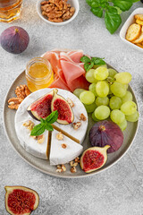 Camembert, bree cheese, walnuts, fresh figs, grapes, prosciutto and honey on a plate on a concrete background. Charcuterie plate. Top view