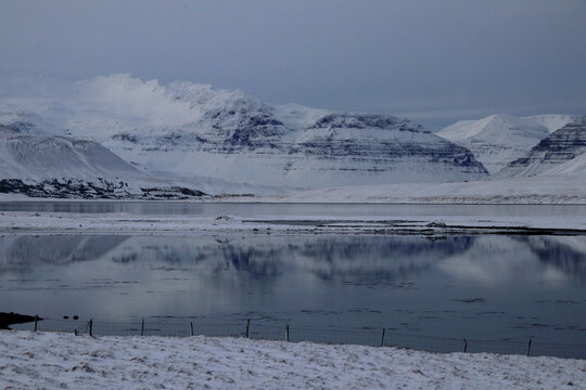 Snow-covered mountains reflected in calm water under clear winter sky