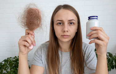 Sad woman holding hairbrush with lost hair and a bottle of vitamins