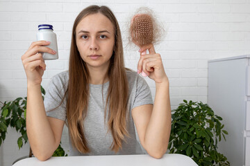 Sad woman holding hairbrush with lost hair and a bottle of vitamins