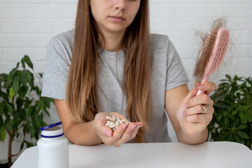 woman holding hairbrush with lost hair and a bottle of vitamins for baldness