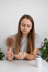 woman holding hairbrush with lost hair and a bottle of vitamins for baldness