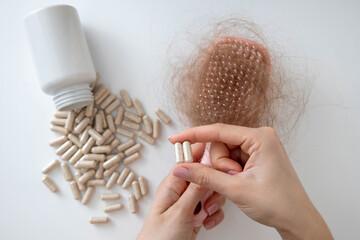 Woman holding hair loss vitamins, hairbrush with fallen hair and supplement capsules on white background