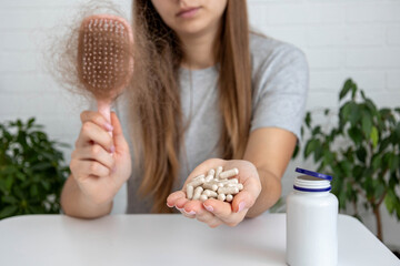 woman holding hairbrush with lost hair and a bottle of vitamins for baldness