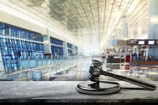 Gavel for justice and the law in an airport departure hall, suggesting a global travel or international legal issue. Concept of rules, compliance, and governance