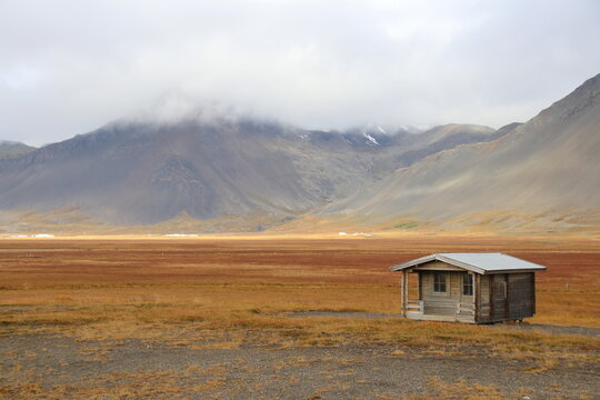Wooden cabin in golden grassland with misty mountains and low clouds in remote landscape