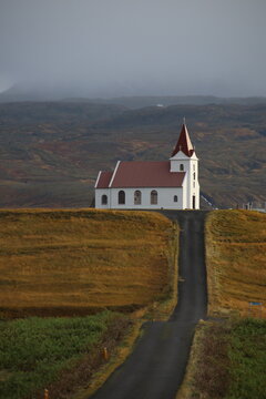 White church with red roof on hilltop surrounded by autumn fields and misty mountains