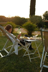 Relaxed woman enjoying a glass of white wine and outdoor dinner in a sunlit Mediterranean garden at sunset