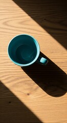 A teal mug on a wooden surface with sunlight creating shadows.