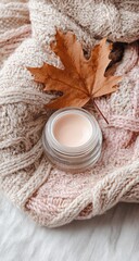 Autumnal skincare cream atop knit, maple leaf accent, cozy