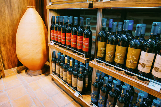7 November 2025, Tbilisi Airport, Georgia: wine bottles, including Kisi and Alazani Valley, on wooden shelves next to a traditional qvevri