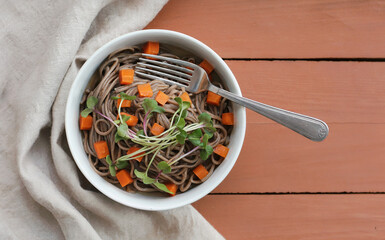 Buckwheat Soba Noodles Bowl with Carrots and Microgreens on Wooden Table